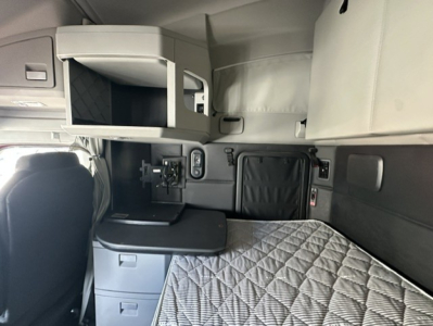 Cabin area of a 2023 Kenworth T680 sleeper, showing bunk bed with quilted mattress, side storage drawers, and upper compartment in view.