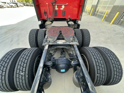 Kenworth T680 truck chassis rear view showing tandem axle with dual tires and fifth wheel, red cab in background.