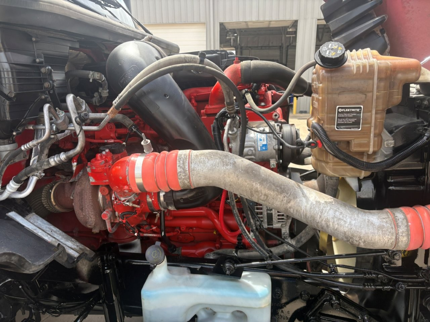 Engine bay of a 2022 International LT showing red engine, hoses, coolant reservoir, and brown power steering reservoir.