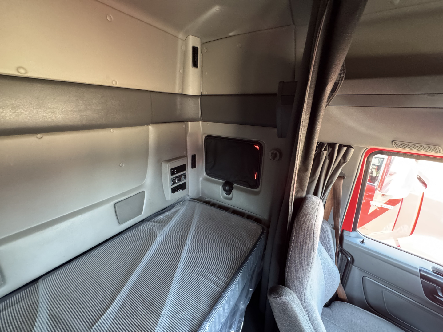 Interior sleeper cab of a 2022 International LT showing a sleeping berth with grey panels, small side storage, and window view; cab corner and seat visible.