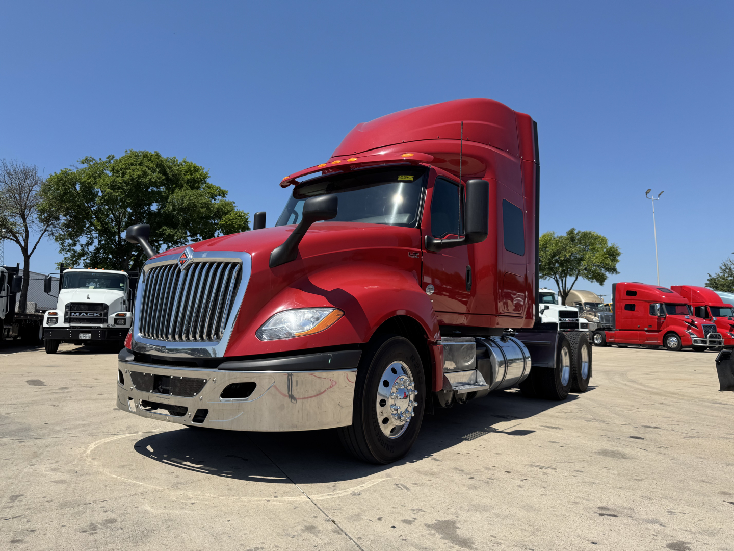 Truck cab in a dealership lot: 2022 International LT tractor with red cab, chrome front bumper, side mirrors, and sleeper cab visible; other trucks in background.