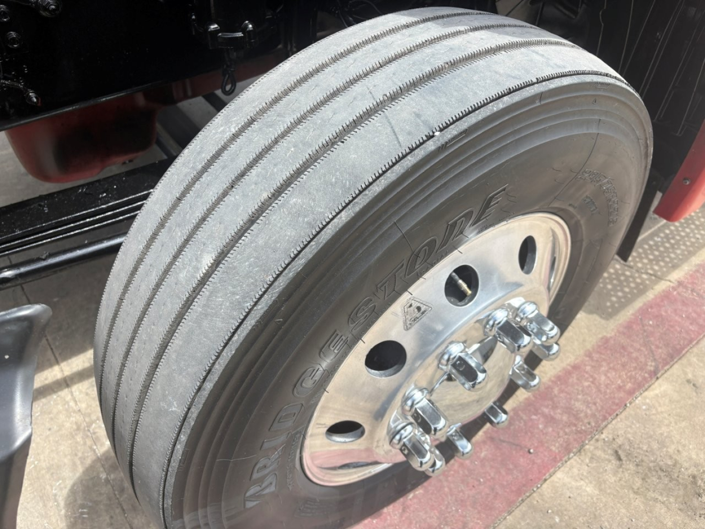 Truck wheel close-up showing steering axle dual tires and chrome lug nuts on a commercial tractor trailer.
