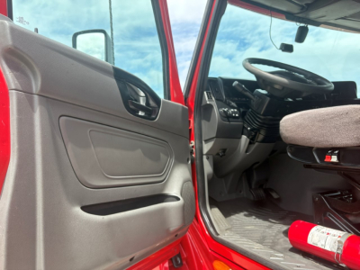 Truck cab interior of a red 2022 International LT seen from the driver side with door open; steering wheel, dashboard, and driver seat visible; a fire extinguisher mounted near the floor.