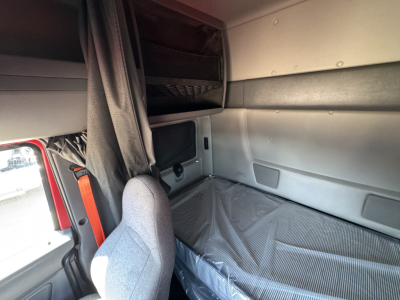 Truck sleeper cab interior with upper bunk and window, gray seat, and storage panels visible.