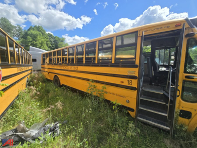 School bus side view with open door showing 'Fort Wayne Community District' decal and bus number 18, blue sky with clouds.