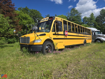 Yellow Freightliner B2 school bus parked in grass with trees in background, front grille and stop sign visible.