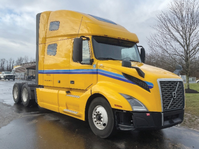 Volvo truck in yellow with blue stripe, sleeper cab, side view showing VIN/stock not visible, no text readable due to angle.