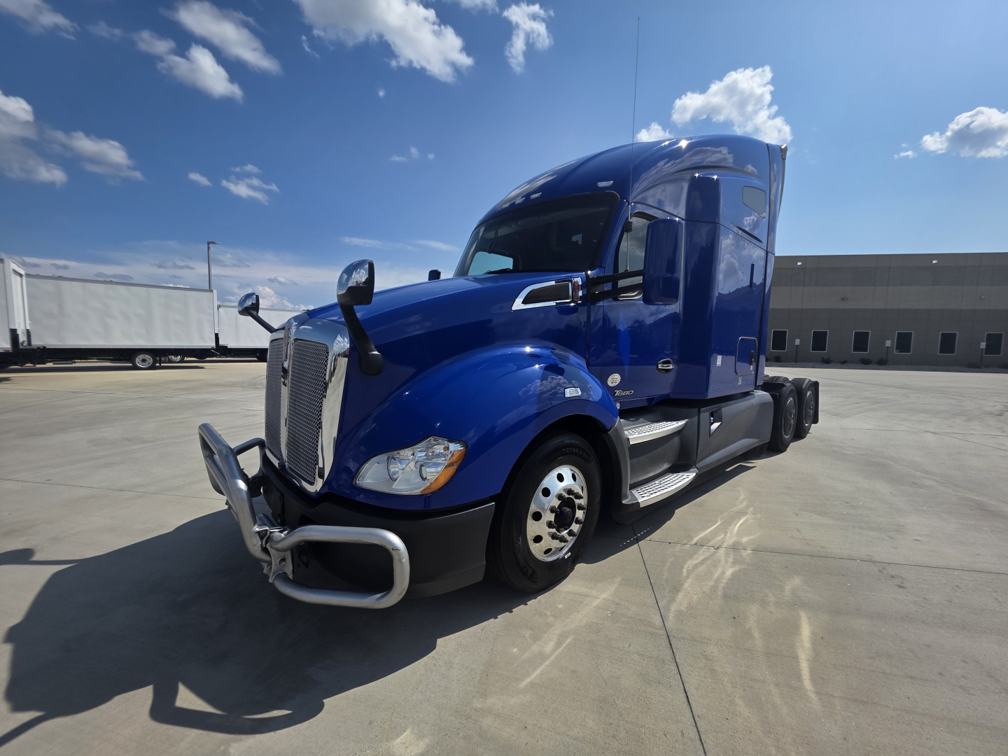 Kenworth T680 truck in blue, front-left view showing chrome bumper guard and sleeper cab with side mirrors.