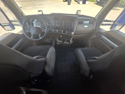 Kenworth T680 cab interior showing steering wheel, driver and passenger seats, dashboard with gauges, central control panel, and large windshield.