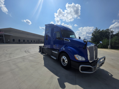 2021 Kenworth T680 blue truck in a parking lot, side view of cab with chrome bumper and aerodynamic mirrors.