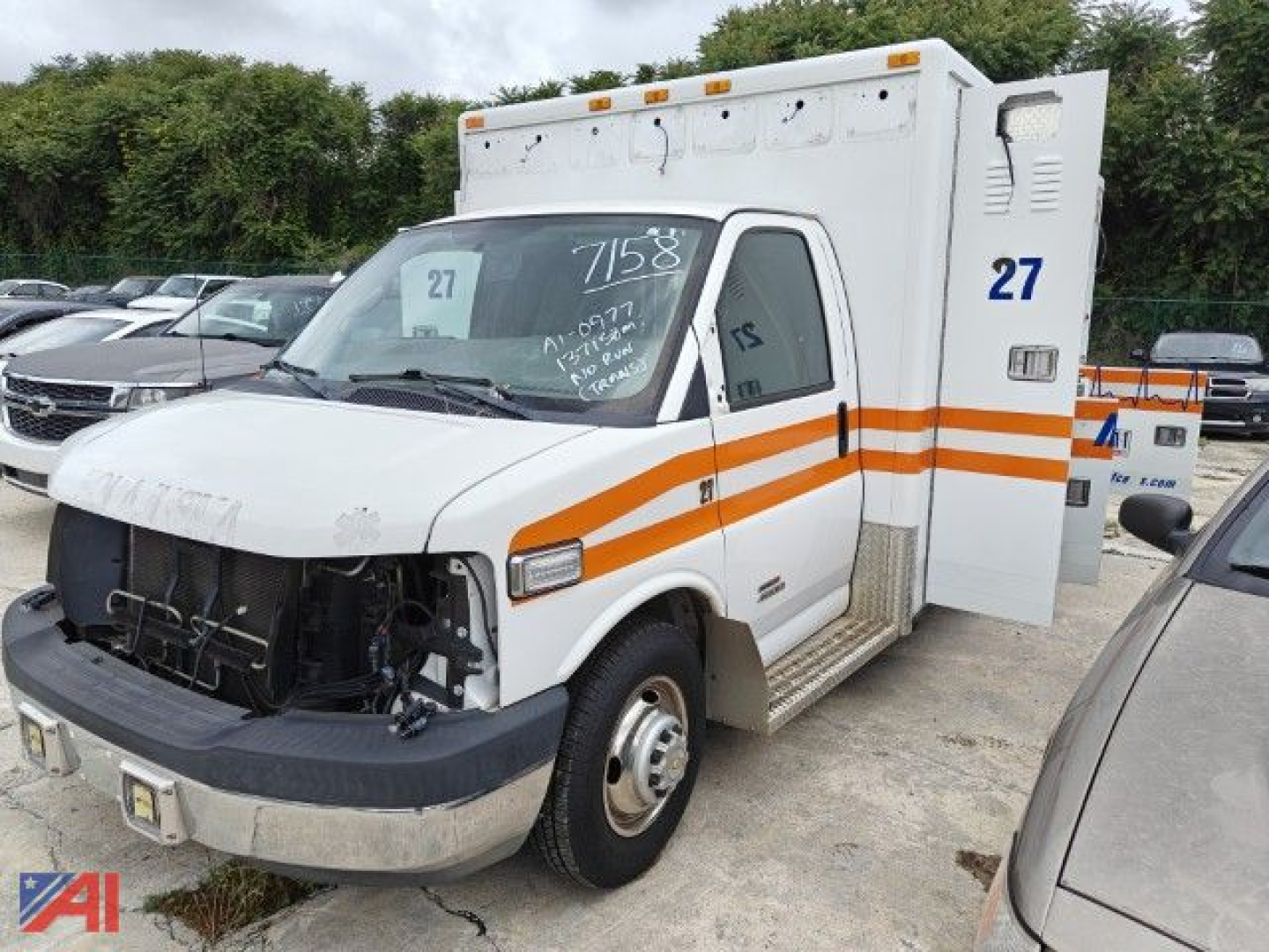 Ambulance body of a white 2016 Chevrolet Express ambulance with orange stripe, front bumper missing grille, side door, rear compartment, number 27 on door and decal 75.58 on windshield.