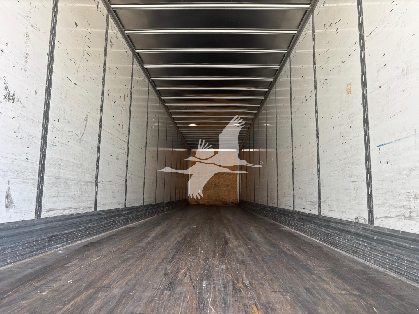 Trailer interior showing long empty cargo area with wooden floor, metal sidewalls, and ceiling beams.