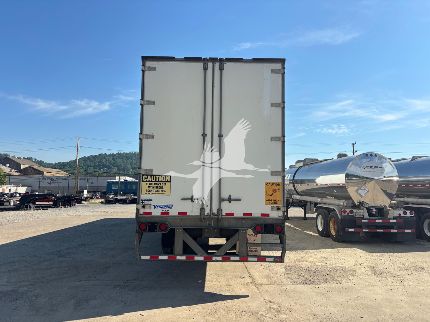 Rear view of a 2017 Vanguard VXP trailer in a lot, dual rear doors, CAUTION and warning stickers, reflective tape along bumper, and other trailers in the background.