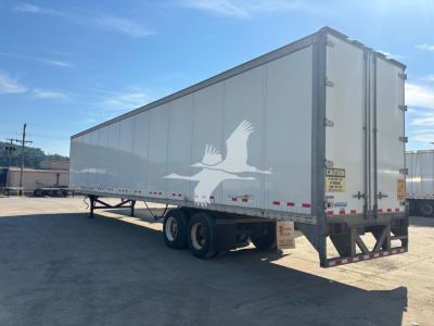Trailer side view of a Vanguard VXP box trailer with a large white graphic of a flying crane. Dual rear doors, side marker lights, and labeling/CAUTION sticker near the back.