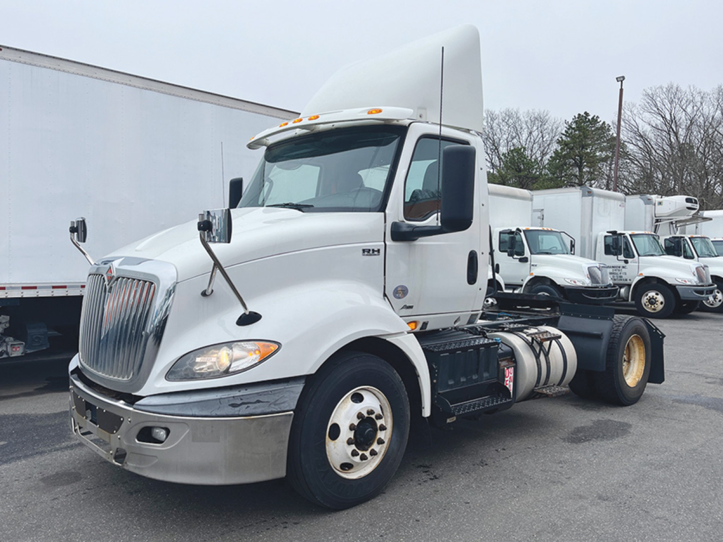 International RH613 daycab truck with white cab and dual rear wheels in a row of trucks, front left view.