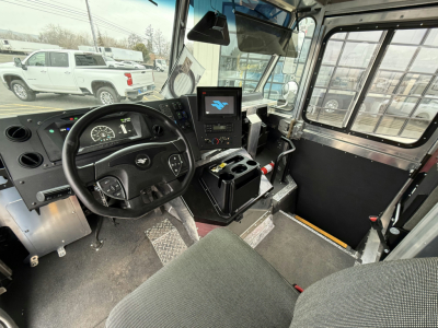 Truck cab interior showing steering wheel, dashboard, and center touchscreen in Harbinger S524 step van. Visible pedals, gear area, and metal steps.