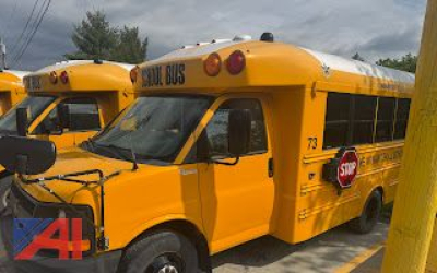 Two yellow Chevrolet express school buses parked side by side, front bus shows 'SCHOOL BUS' lettering on top, stop sign extended on side, number 73 near rear, blue A1 logo overlay on left front of image.