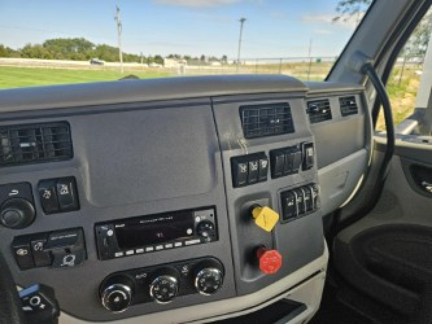 Peterbilt 579 truck dashboard interior view showing control switches, knobs, and yellow and red handles in the console; partial windshield and driver seat visible.