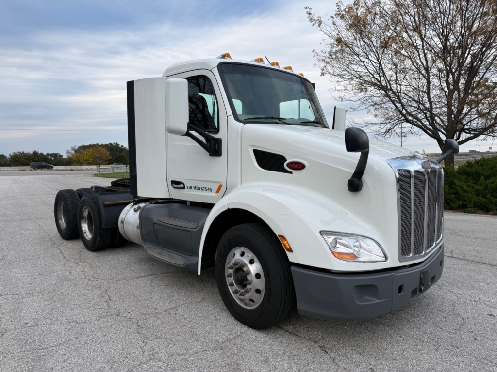 Peterbilt 579 daycab truck side view showing front grille, cab, and wheel. Visible text includes Peterbilt emblem on the hood and side badge along the door area. No other legible markings visible.