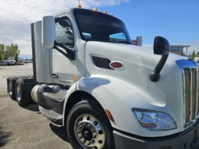 Peterbilt 579 conventional daycab truck, white exterior, front-left view showing cab with large chrome grille, side mirrors, and dual rear axles.