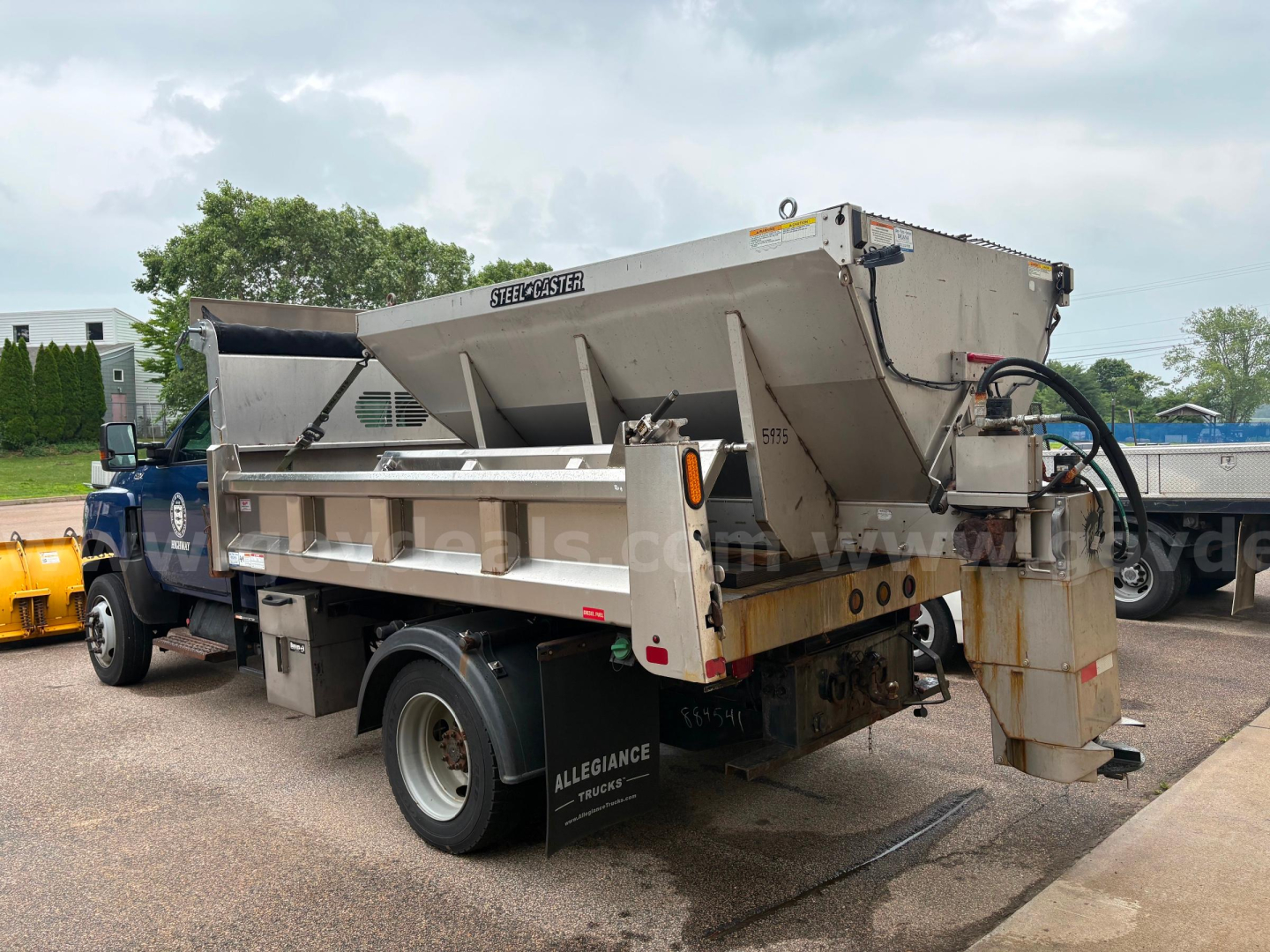 Dump truck rear view showing large steel dump bed with hydraulic actuator and tailgate, side mirrors, and dual rear wheels.