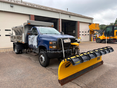 Dump truck with blue cab and yellow snow plow attachment at front, International CV515, visible in service bay.