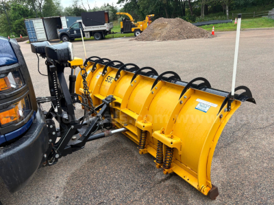 Snow plow attachment connected to a truck, yellow snow blade with black coil springs and mounting frame visible.