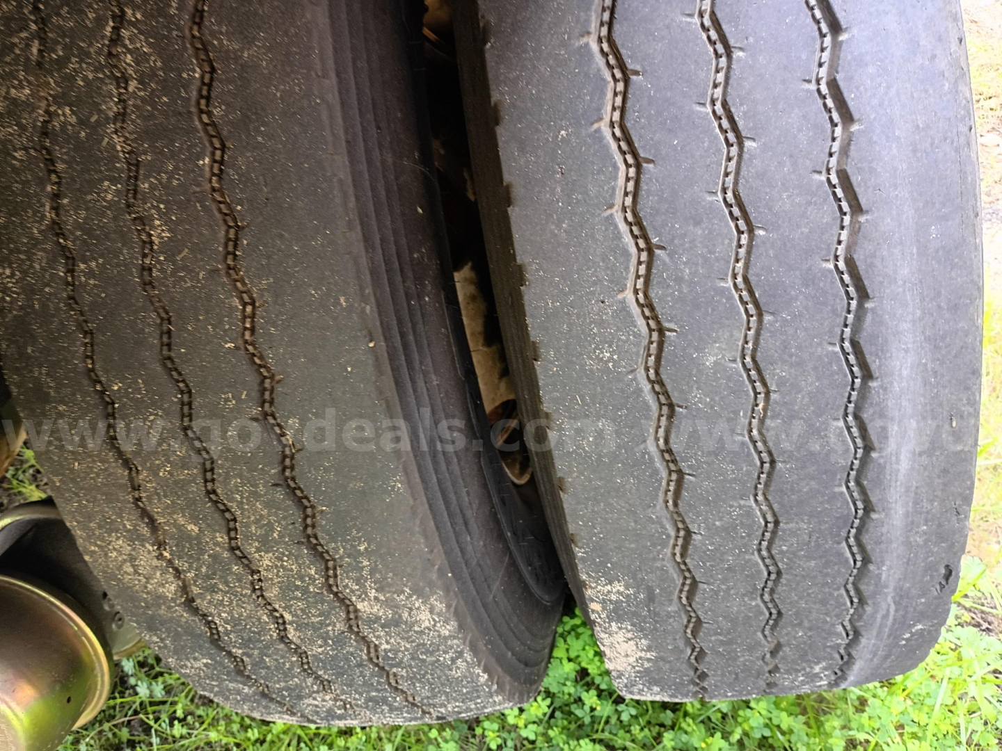 Two rear tires of a Freightliner 114SD truck showing worn tread and mud, with partial wheel well and chassis visible.