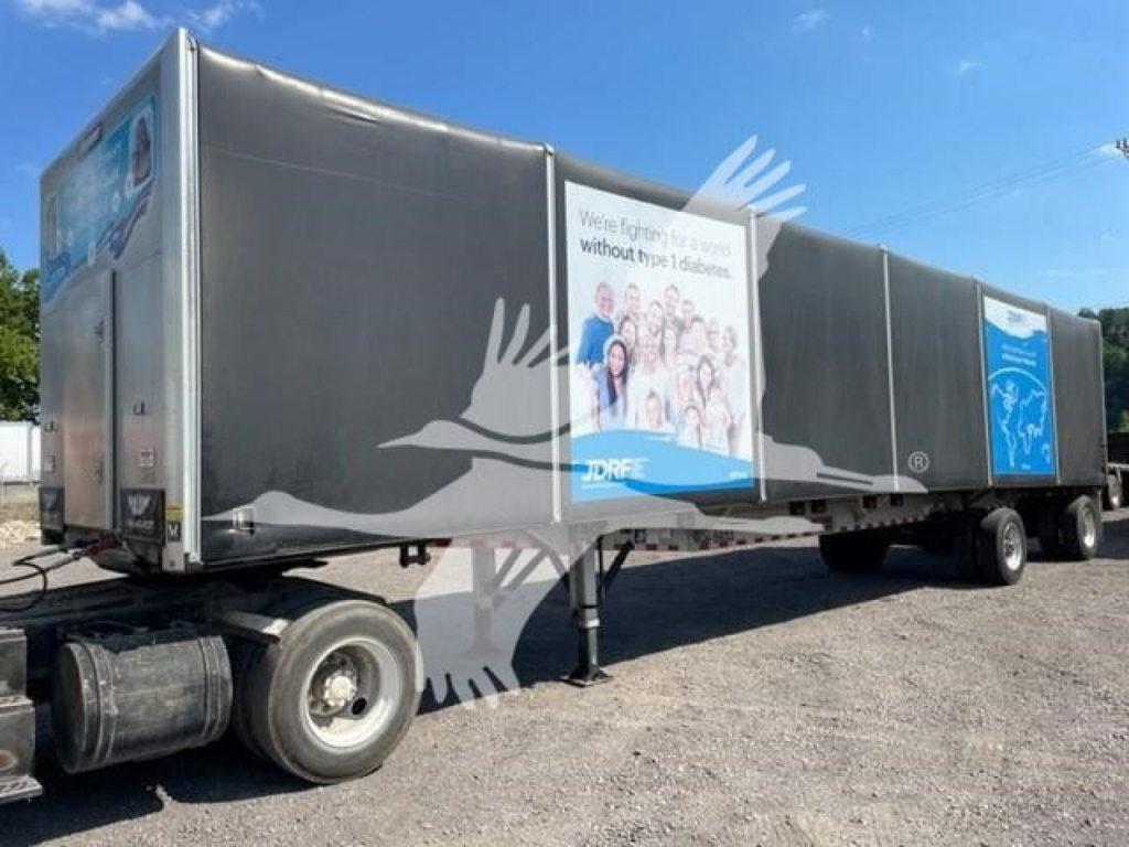 Trailer side view showing 2021 Reitnouer Bubba curtainside trailer with stock banners and DOT sticker, black exterior, spray painted logos.