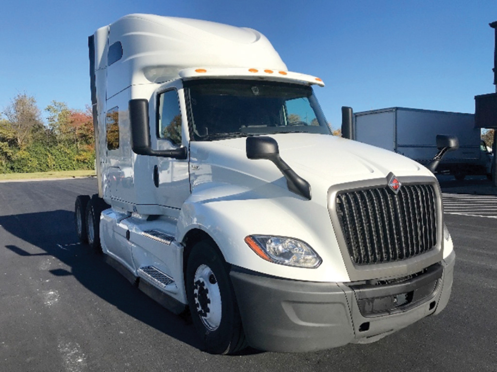Truck cab front-left angle showing International LT series emblem and large vertical grille; white Sleeper tractor with black bumper; headlights and side mirror visible.