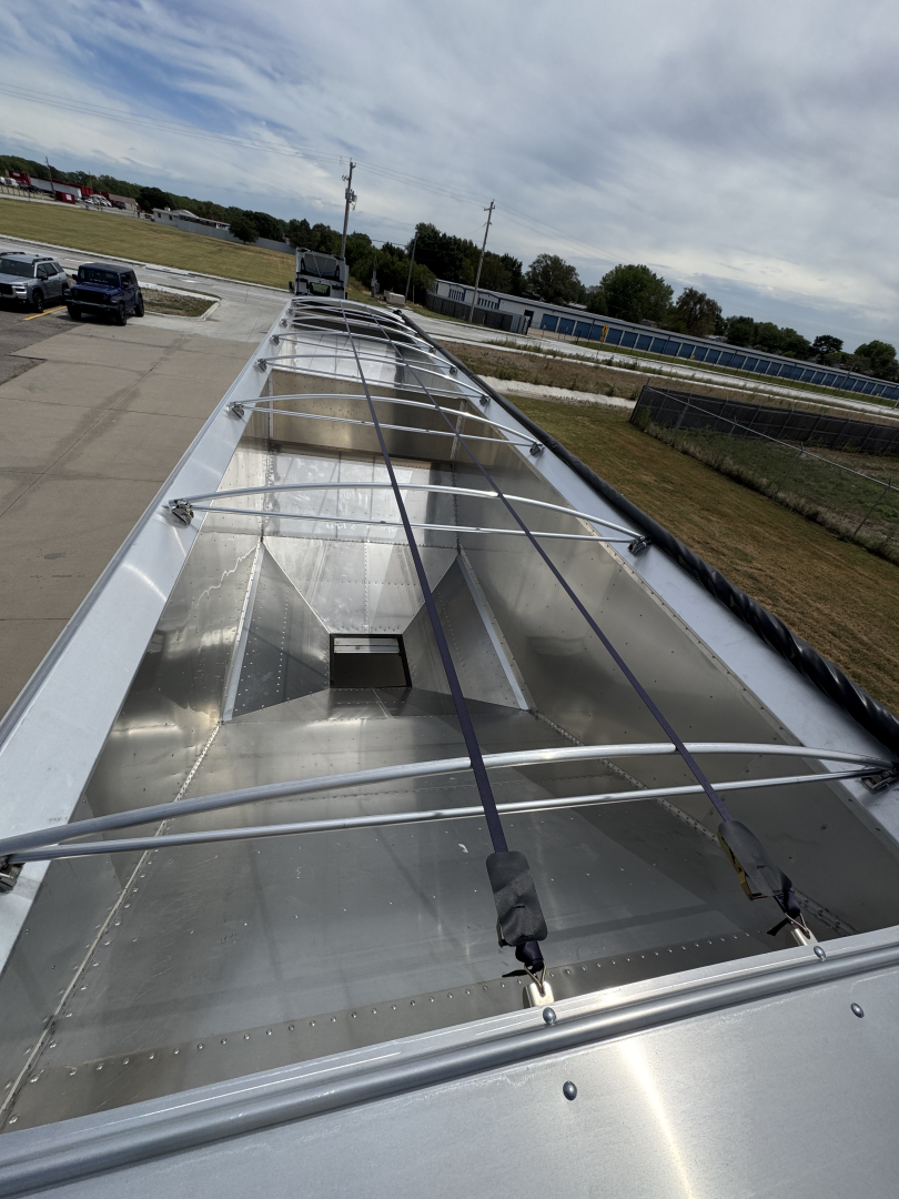 Trailer hopper interior showing corrugated aluminum sidewalls and tie-down straps along the top with reflections on metal surface.