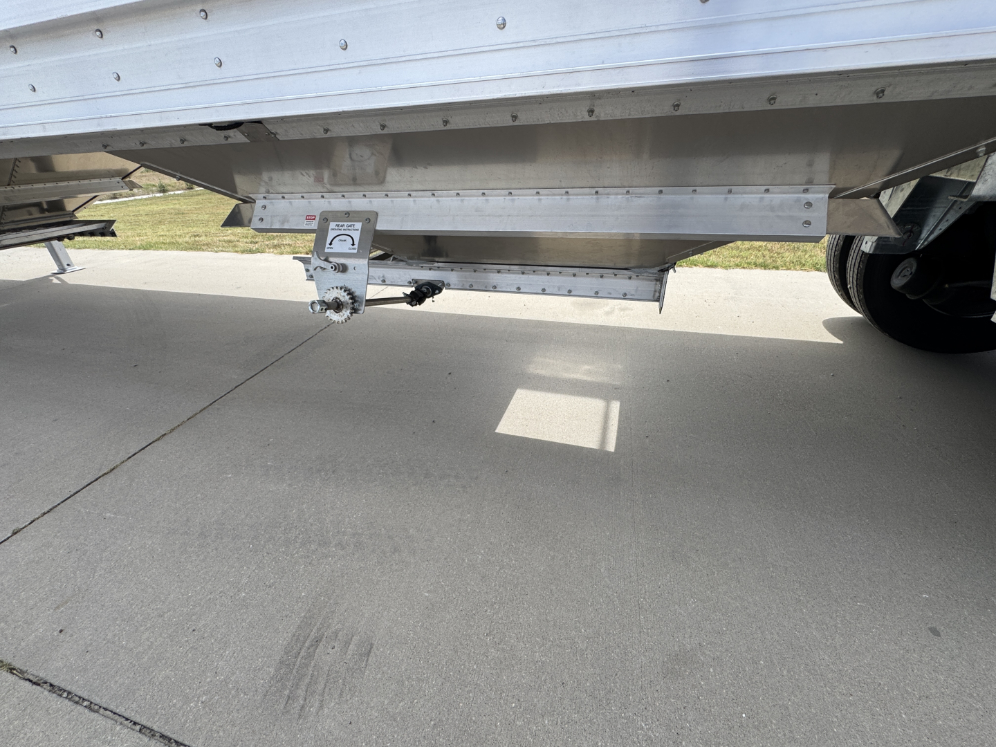 Trailer underbelly showing underside of 42' aluminum grain hopper with corrugated sidewalls and tandem axle. Visible components include a leveling jack and mounting hardware.
