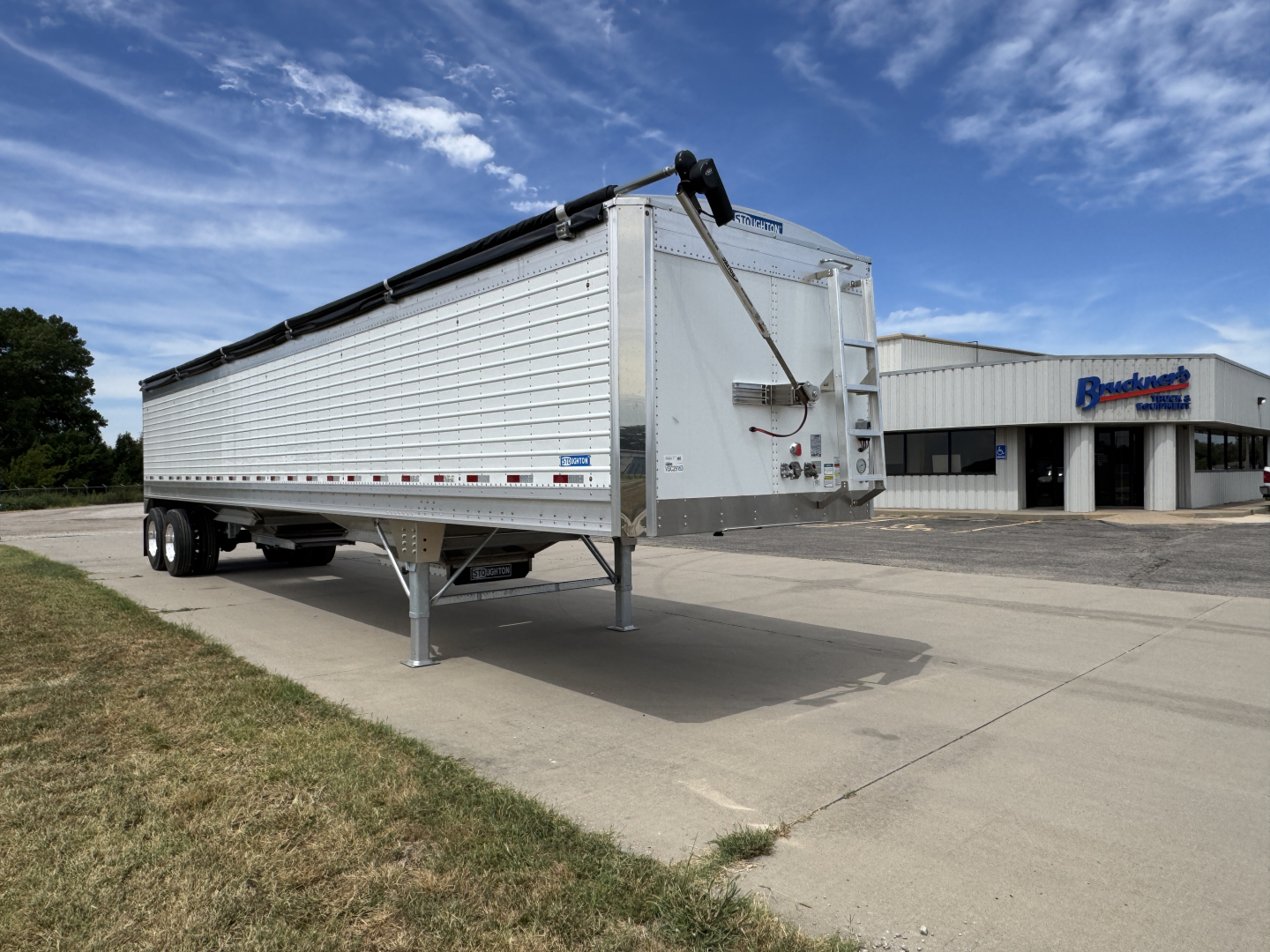 Grain hopper trailer with 42-foot aluminum corrugated sidewalls and dual rear axles, front hitch and landing legs, parked on pavement.
