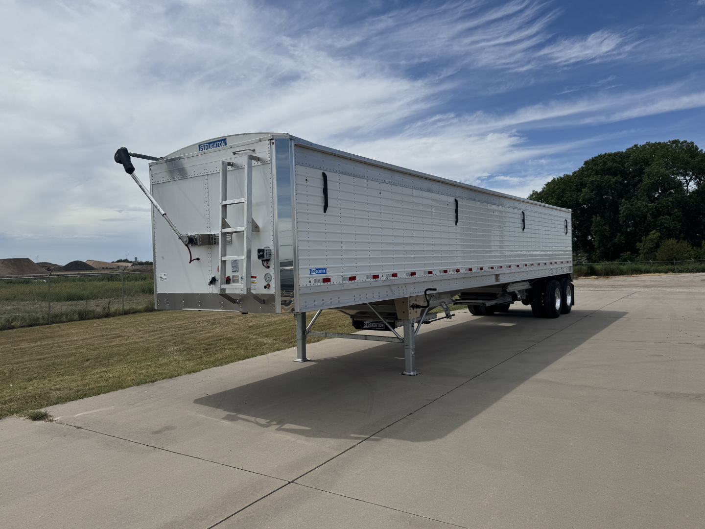 Trailer side view showing 42' aluminum hopper with corrugated sidewalls and front landing gear. VIN tag visible, Stoughton hopper trailer in a parking lot.
