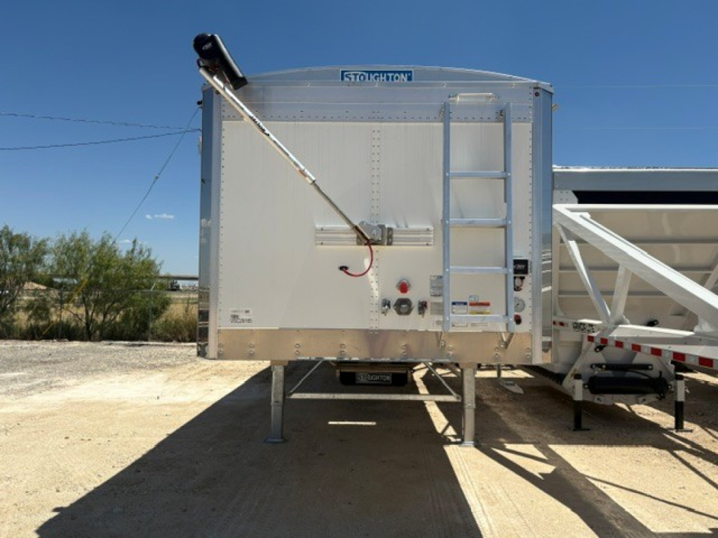Stoughton 42' aluminum grain hopper trailer with corrugated 74" sidewalls, front view showing hitch and ladder, VIN visible on tag.