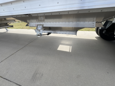 Trailer underbelly showing underside of 42' aluminum grain hopper with corrugated sidewalls and tandem axle. Visible components include a leveling jack and mounting hardware.