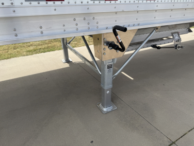 Semi-trailer hopper leg and undercarriage showing corrugated sidewall, support frame, and landing gear foot with a crank handle visible.
