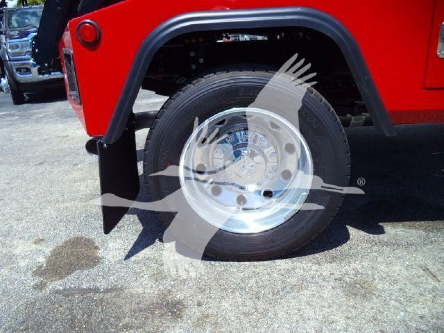 Truck wheel and fender area showing a polished aluminum wheel with lug nuts under a red fender; part of a heavy-duty truck with black fender flare.