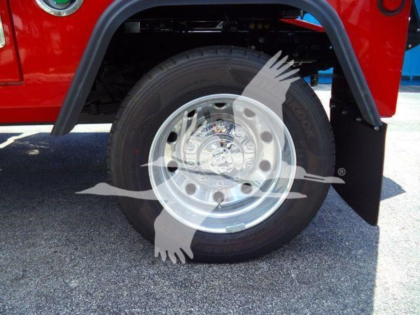 Truck wheel and tire assembly with aluminum rim under fender, red body panel visible, black mud flap nearby.