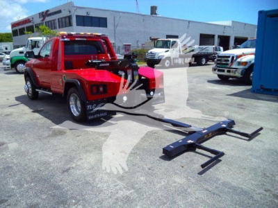 Red Ram 4500 pickup in a lot with a tow winch attachment lying on the ground in front. The tailgate displays a logo and the background shows service center buildings and other trucks.