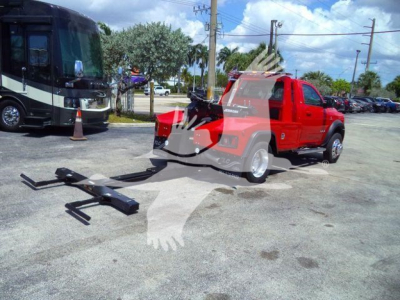 Red Ram 4500 pickup with a damaged tow hitch assembly on the ground beside it, winch equipment and black forks laid out in front, service lot background with other vehicles.