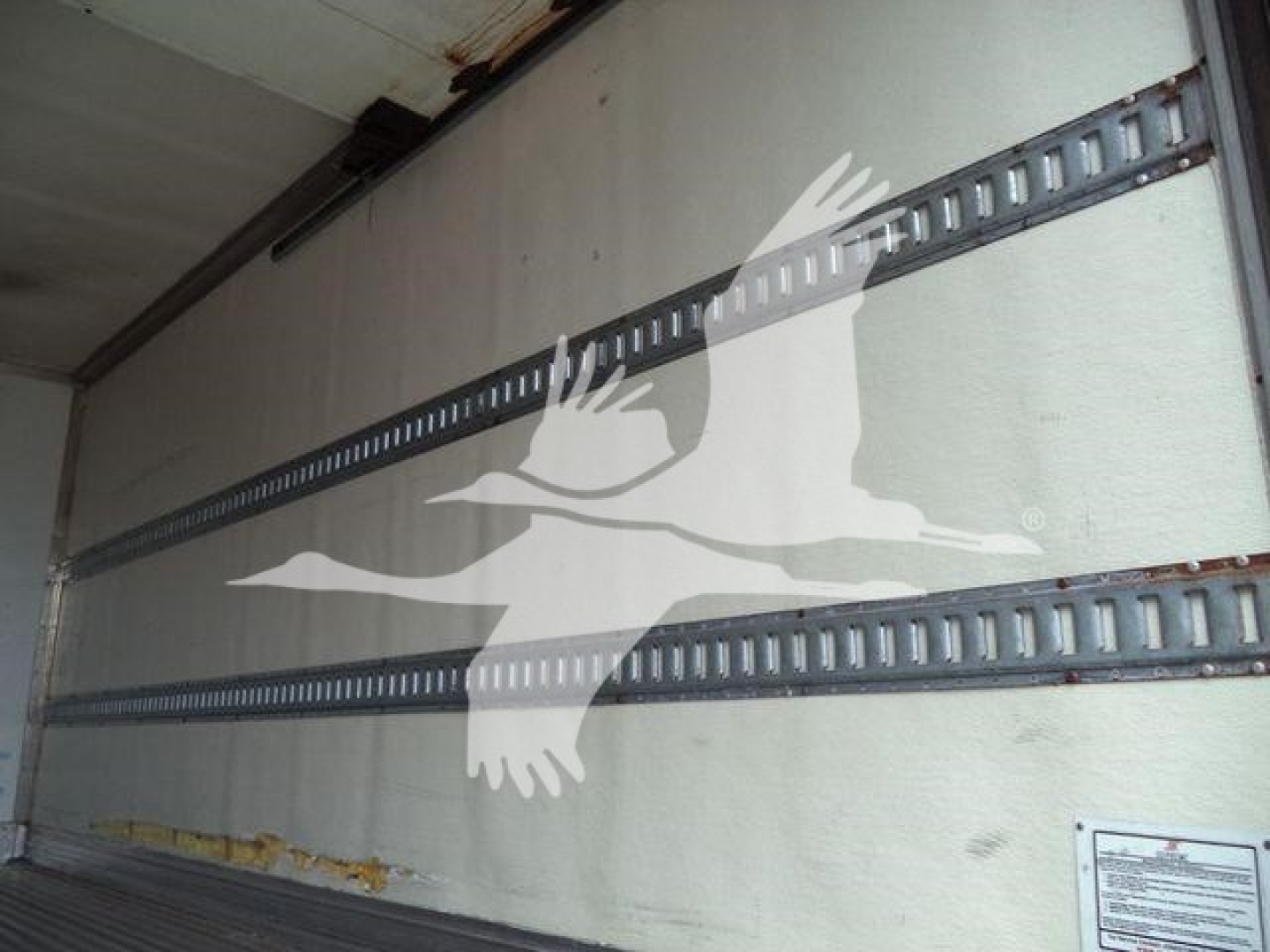 Truck trailer interior showing side rails and a reflective logo, with a white bird-like graphic on the wall.