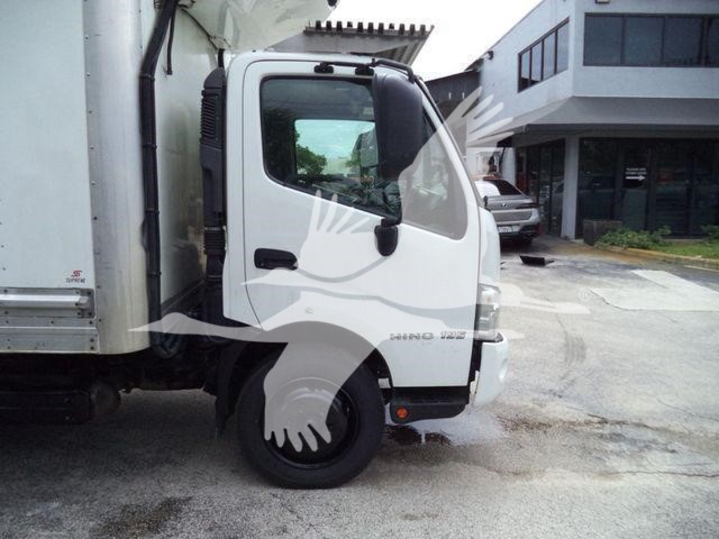 Truck cab front view showing 'HINO' badge on door and side mirror, with a refrigerated box attached; visible wheel and fender.