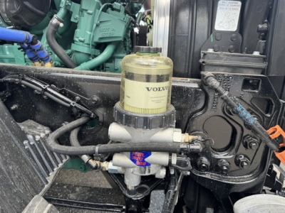 Volvo engine bay showing fuel/water separator with clear plastic canister and hoses in front of engine block.