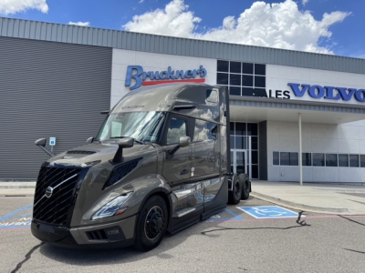 Volvo VNL64T860 tractor-trailer in front of dealership, dark gray cab, long sleeper, branding on building shows Volvo and Bruckner's.
