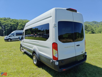 Ford Transit van with wheelchair lift from rear-right perspective showing tall body, dark rear windows, and outside field background.