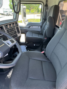 Mack GR64F truck cab interior with steering wheel, dashboard gauges, and driver seat; front passenger seat visible.