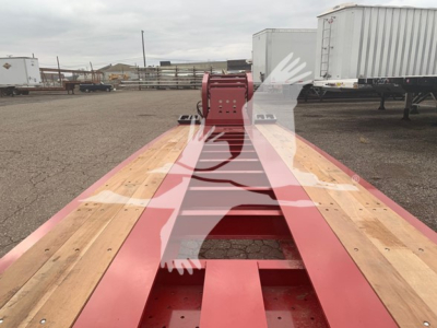 Lowboy trailer frame showing red hydraulic landing gear box and wooden deck sections with cutouts and framing.