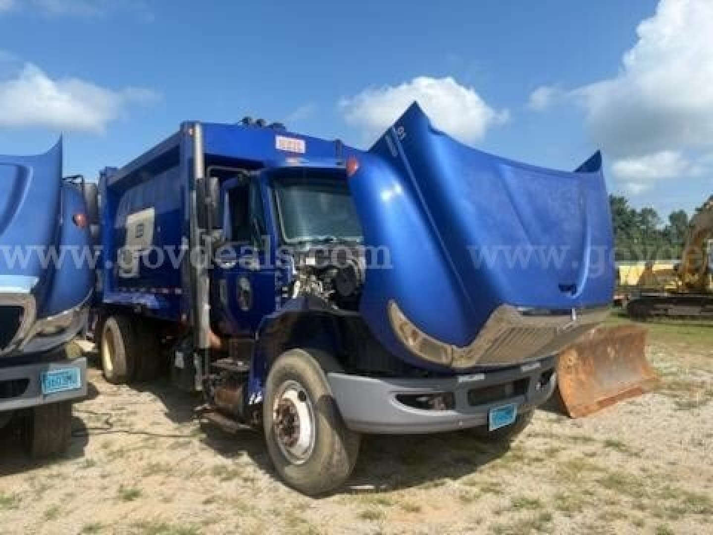 Truck with cab and front end detached, blue International 4400 garbage truck body upright in yard. Visible text on side: www.govdeals.com watermark across image. Front shows engine bay exposed.
