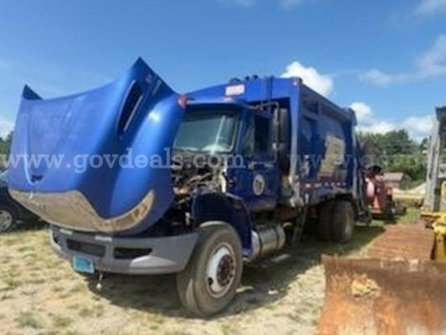 Truck front hood open with blue garbage truck body; side shows white text watermark; no clear close-up of labels or specs visible.